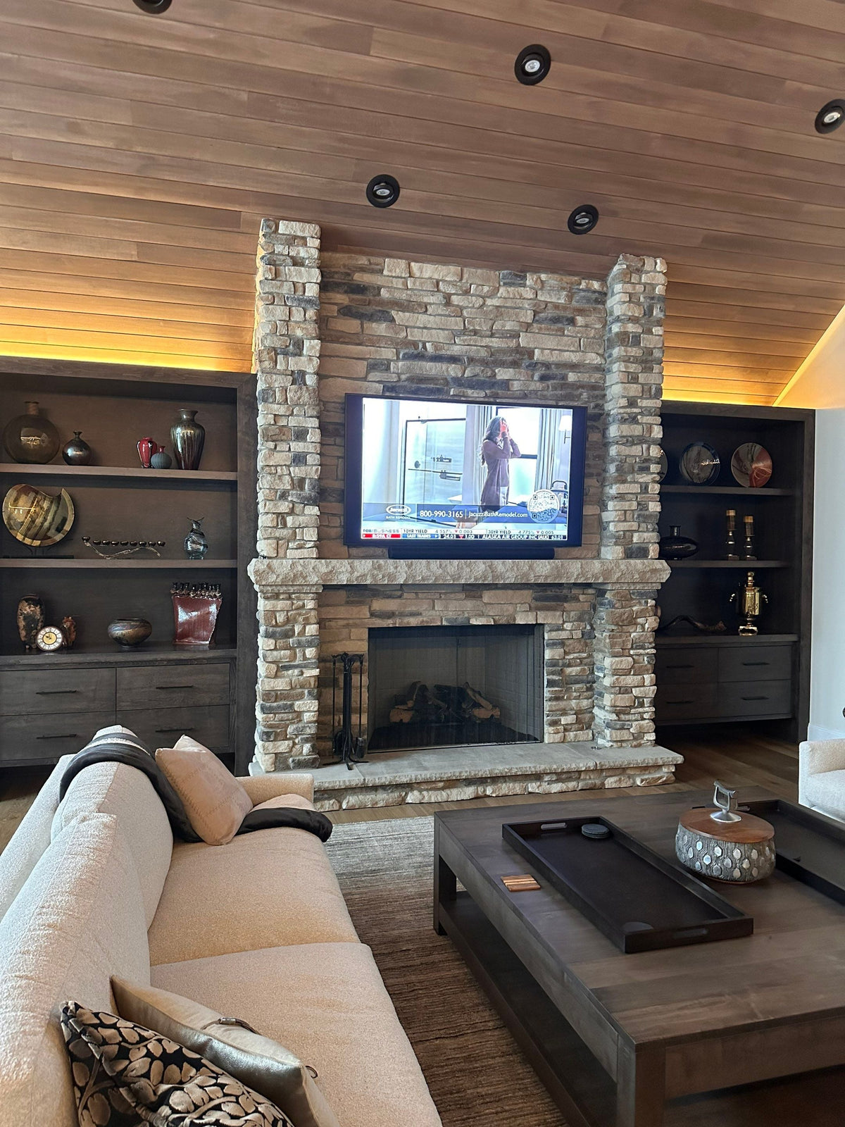 TV above a stacked-stone fireplace with built-in shelving
