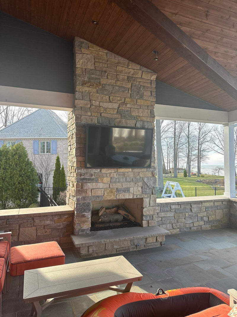 Outdoor TV over a stone fireplace on a covered patio