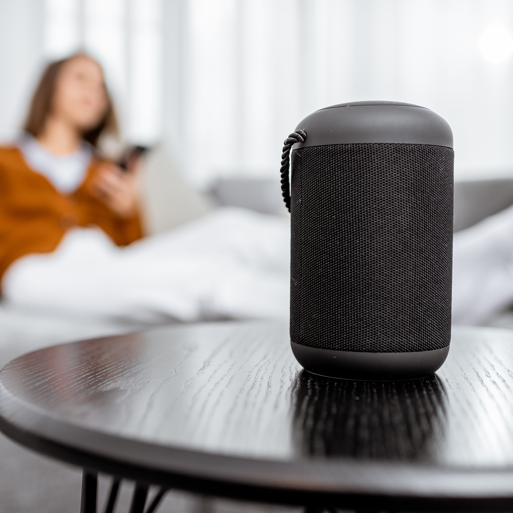 Black portable speaker on a table with a blurred person sitting on a couch in the background