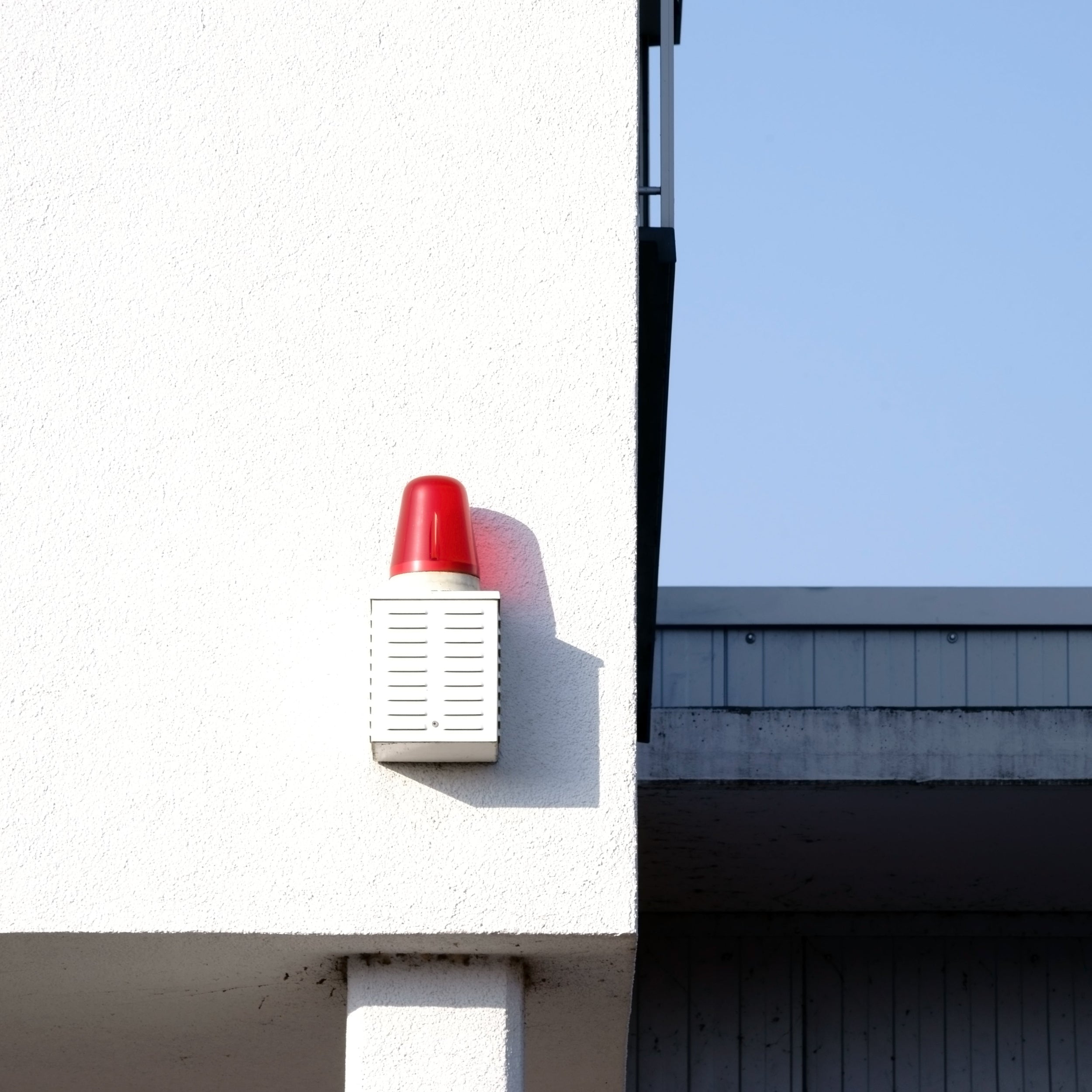 Red and white fire alarm on a building exterior with a clear sky.